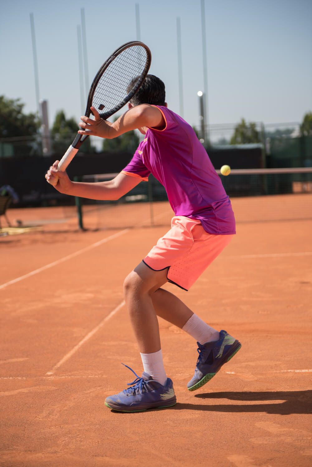 Junger Tennisspieler schlägt eine einhändige Rückhand beim Sparring 1-1 auf Sand.